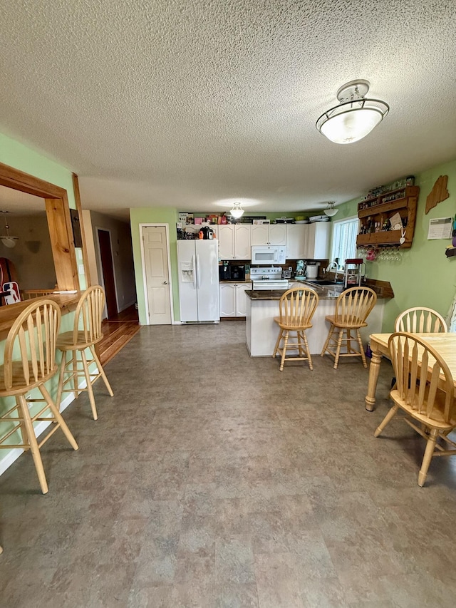 12 Grace Snow Dr, Glenburn, ME 04401 - kitchen with white appliances, a peninsula, white cabinetry, dark countertops, and a kitchen breakfast bar