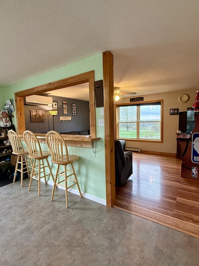 12 Grace Snow Dr, Glenburn, ME 04401 - kitchen with a textured ceiling, a wall unit AC, ceiling fan, a breakfast bar area, and baseboards