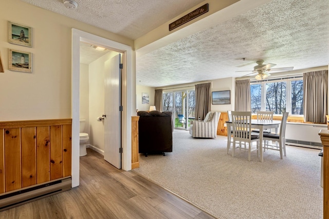 1373 Post Rd Unit 4A, Wells, ME 04090 - dining area with ceiling fan, a textured ceiling, wood finished floors, a wainscoted wall, and a baseboard radiator