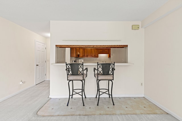 161 Saco Ave Unit 404, Old Orchard Beach, ME 04064 - kitchen with brown cabinetry, a breakfast bar, light countertops, baseboards, and a peninsula