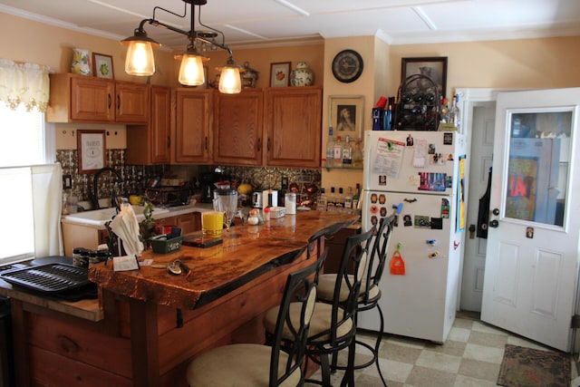 13 Halde St, Waterville, ME 04901 - kitchen featuring freestanding refrigerator, light flooring, brown cabinets, backsplash, and ornamental molding