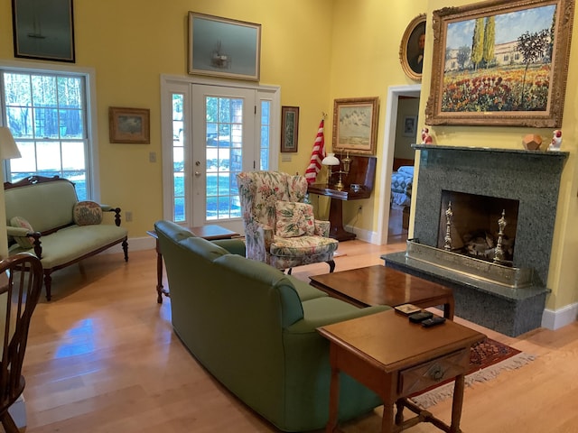 living area featuring a high end fireplace, baseboards, light wood-style flooring, and a towering ceiling