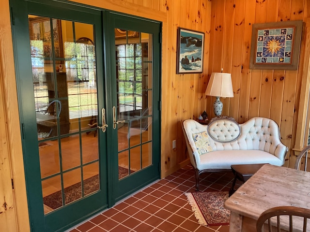 living area with french doors, wood walls, and dark tile patterned floors