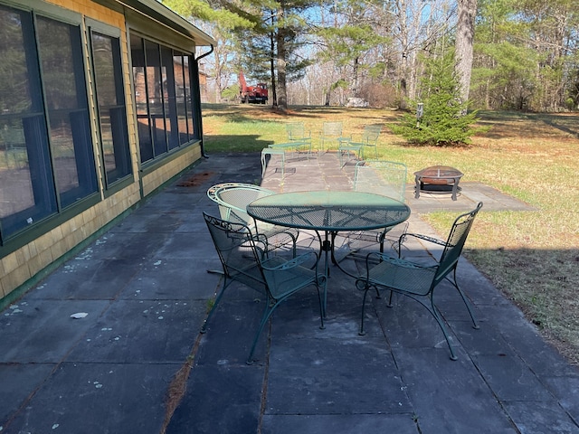 view of patio with a fire pit, outdoor dining space, and a sunroom