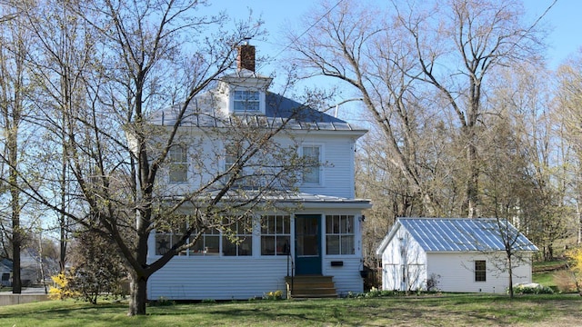 exterior space featuring a lawn, a chimney, an outdoor structure, and a sunroom