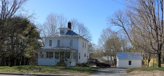 view of front of home with a sunroom, a front yard, a chimney, a standing seam roof, and metal roof