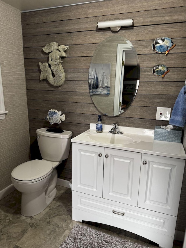 bathroom with vanity, wood walls, baseboards, and toilet