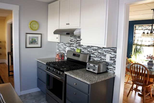 kitchen featuring white cabinets, light stone countertops, decorative backsplash, gas range, and under cabinet range hood