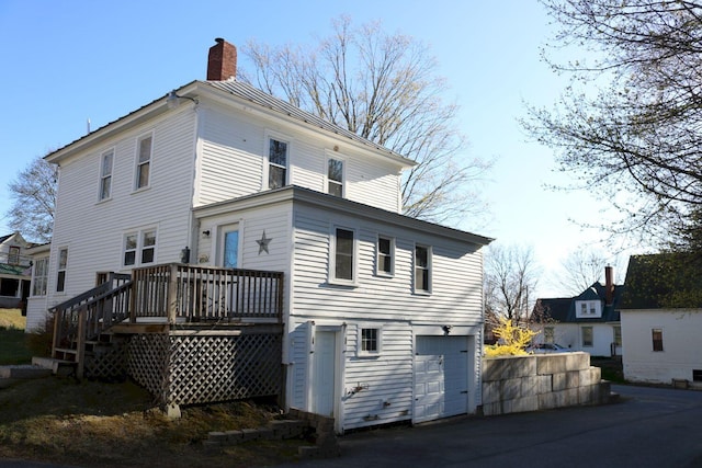 back of house featuring a wooden deck, a chimney, an attached garage, and driveway