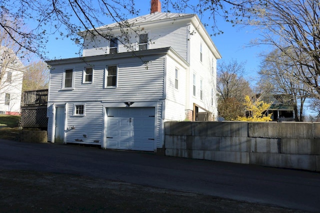 rear view of property with fence, a chimney, and an attached garage