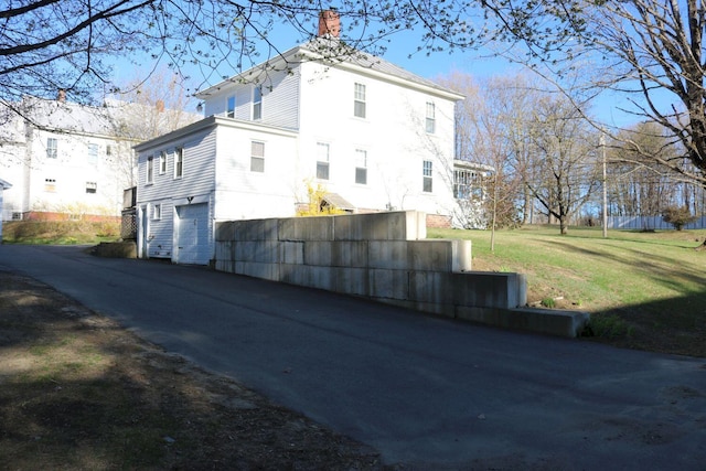 view of side of home featuring an attached garage, a yard, driveway, and a chimney
