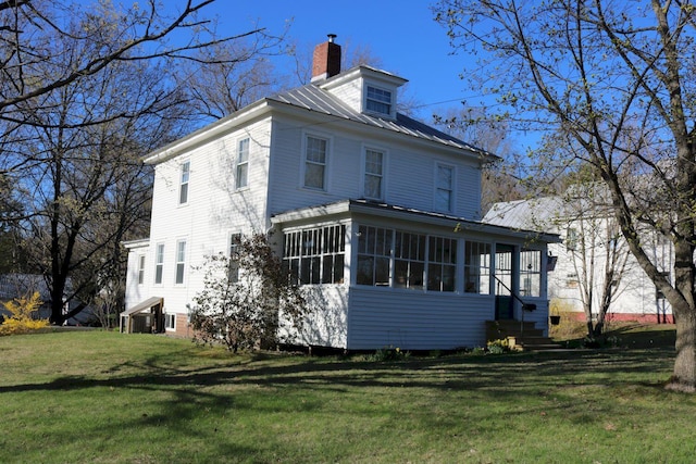 rear view of house with a sunroom, a chimney, a yard, and metal roof