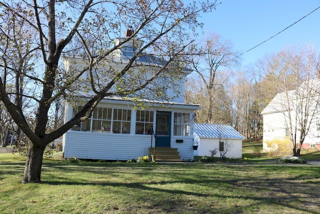 view of front facade featuring a chimney, metal roof, a sunroom, and a front lawn