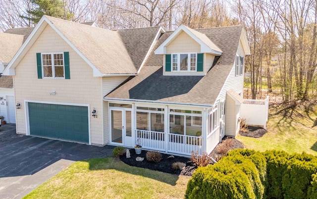 view of front of property with aphalt driveway, an attached garage, a front lawn, a sunroom, and a shingled roof