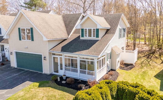 view of front of property featuring driveway, a garage, a front yard, a sunroom, and a shingled roof