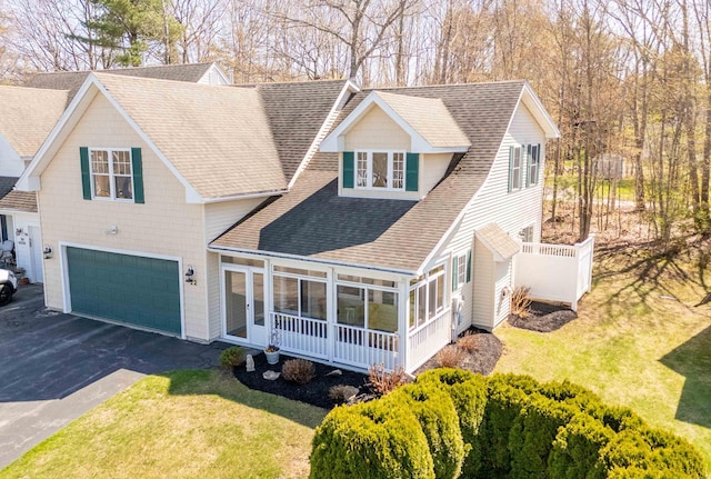 view of front of property featuring aphalt driveway, a garage, a sunroom, roof with shingles, and a front lawn