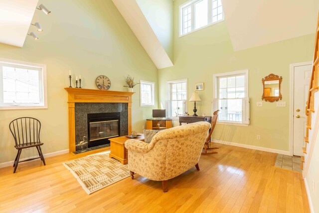 living room featuring light wood finished floors, a tiled fireplace, baseboards, and a high ceiling