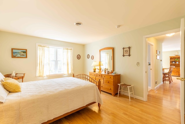 bedroom with baseboards, light wood finished floors, and visible vents