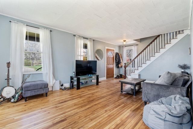 living area featuring stairs, crown molding, baseboards, and light wood-type flooring