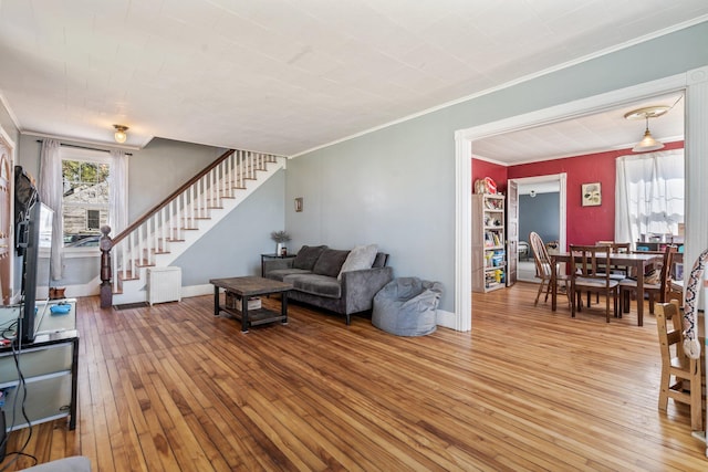 living room with baseboards, ornamental molding, light wood finished floors, and stairway