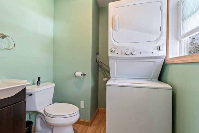 bathroom featuring stacked washer / drying machine, wood finished floors, vanity, baseboards, and toilet