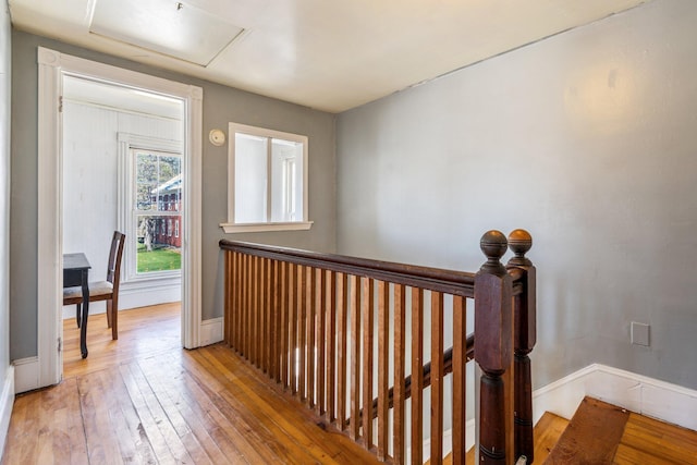 hall featuring baseboards, wood-type flooring, attic access, and an upstairs landing