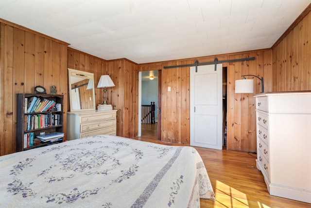 bedroom featuring crown molding, light wood-type flooring, wood walls, and a barn door