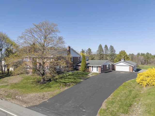 view of front of house featuring a chimney, an outbuilding, a garage, a front yard, and aphalt driveway
