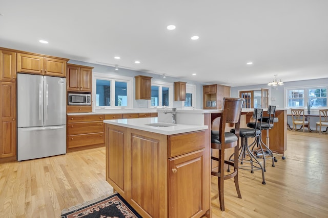 kitchen featuring light wood finished floors, a breakfast bar area, a sink, stainless steel appliances, and brown cabinetry