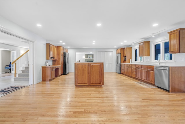 kitchen with a center island, brown cabinetry, light wood-type flooring, light countertops, and appliances with stainless steel finishes