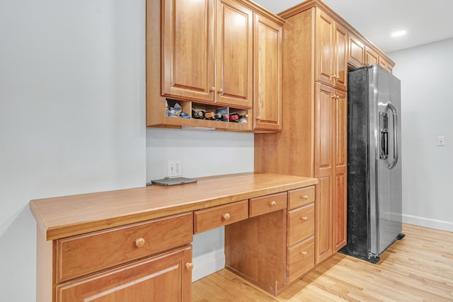 kitchen featuring black refrigerator with ice dispenser, light wood-style flooring, baseboards, built in study area, and light countertops