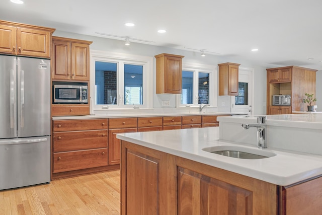 kitchen with light wood finished floors, a sink, brown cabinetry, light countertops, and appliances with stainless steel finishes