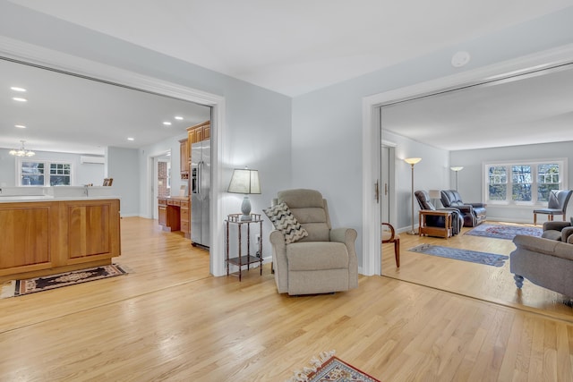 living room with light wood finished floors, baseboards, an AC wall unit, a chandelier, and recessed lighting