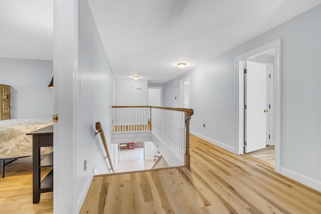 hall with baseboards, an upstairs landing, and wood finished floors