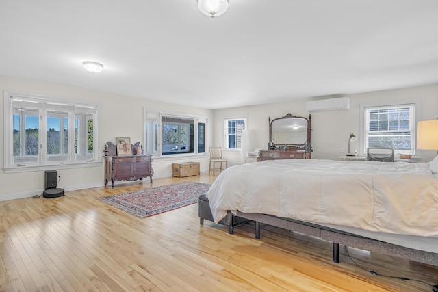 bedroom featuring wood finished floors, baseboards, and a wall unit AC