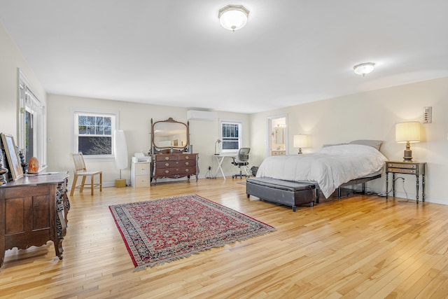 bedroom with a wall mounted air conditioner, baseboards, hardwood / wood-style floors, and multiple windows