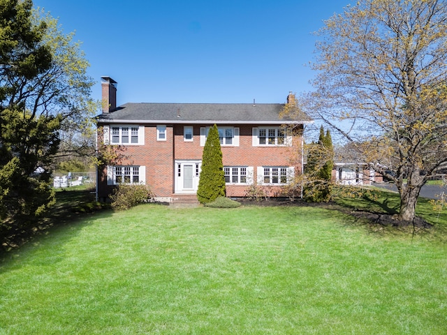 back of house featuring a chimney, brick siding, and a lawn