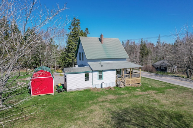 view of front of house featuring metal roof, a chimney, a storage shed, an outdoor structure, and a front lawn
