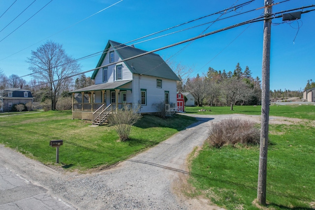 view of property exterior with a lawn, dirt driveway, covered porch, and metal roof