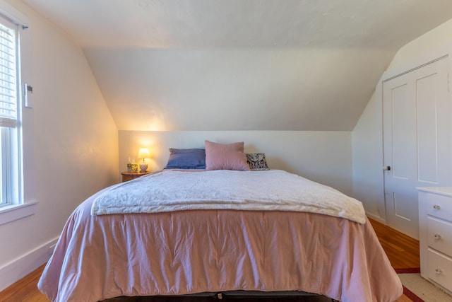 bedroom with multiple windows, lofted ceiling, and light wood-style floors