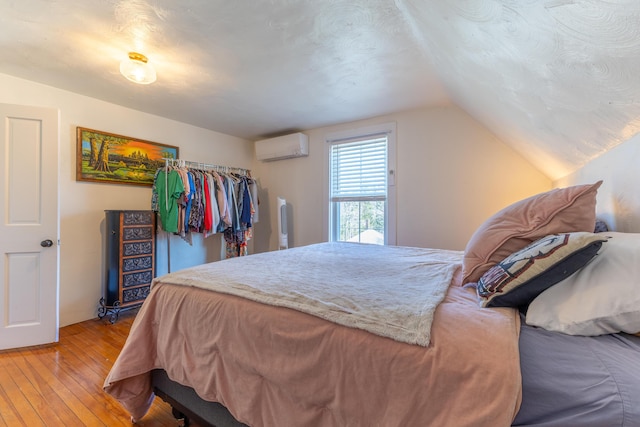 bedroom with an AC wall unit, lofted ceiling, and light wood finished floors