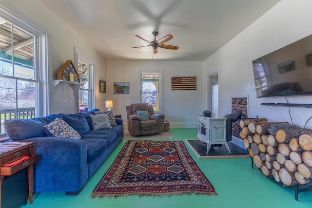 living area with baseboards, a wood stove, and a ceiling fan