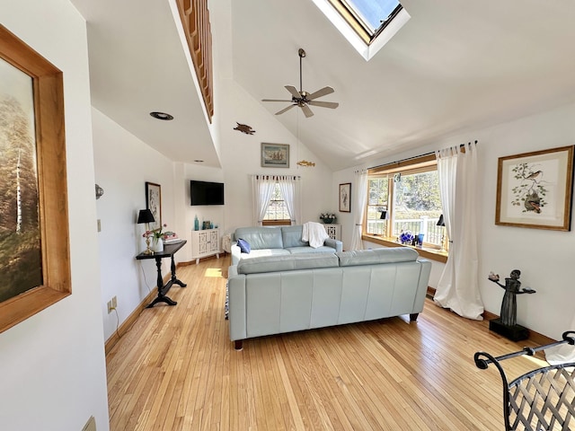 living area with baseboards, high vaulted ceiling, a ceiling fan, light wood finished floors, and a skylight