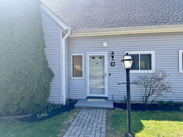 property entrance with a shingled roof and a yard