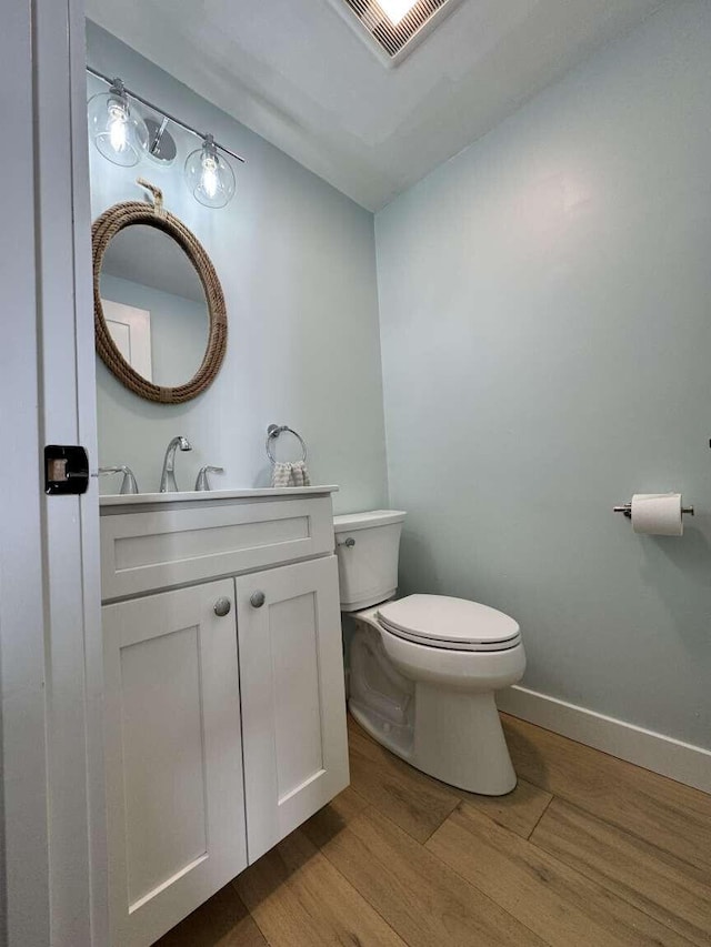 half bathroom with visible vents, vanity, wood finished floors, toilet, and baseboards