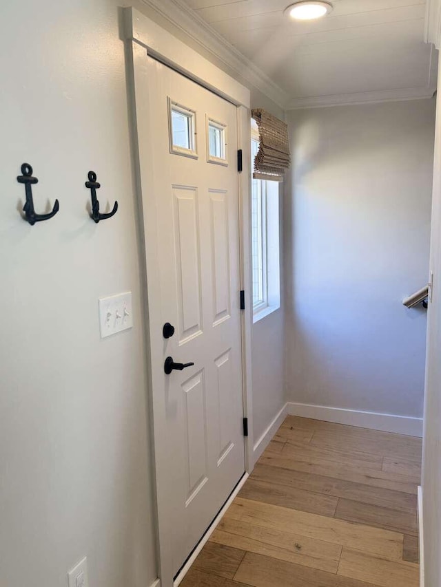 doorway with crown molding, baseboards, and light wood-type flooring