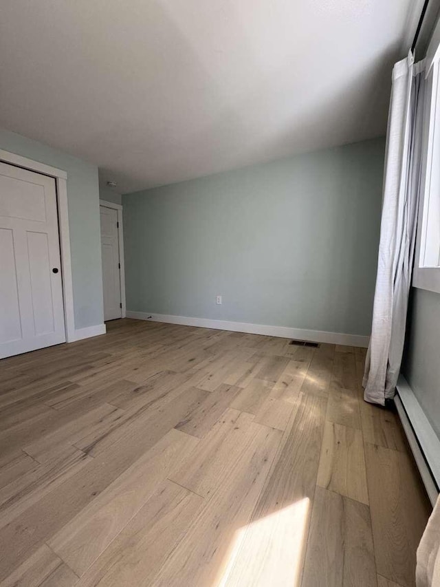 unfurnished bedroom with visible vents, baseboards, a baseboard heating unit, and light wood finished floors