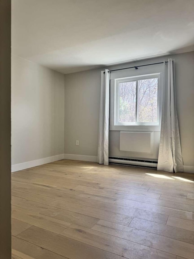 spare room featuring wood-type flooring, baseboards, and a baseboard radiator