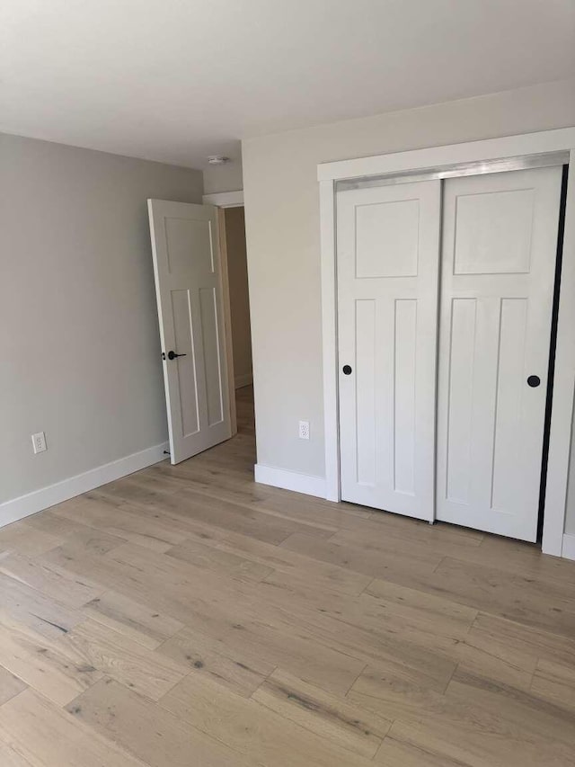 unfurnished bedroom with baseboards, light wood finished floors, and a closet