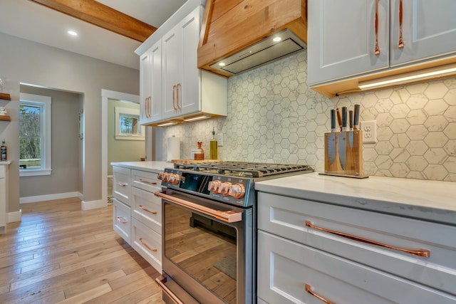 27 Oak Ridge Ter, Arundel, ME 04046 - kitchen featuring stainless steel range with gas stovetop, custom range hood, white cabinetry, baseboards, and light wood-style floors